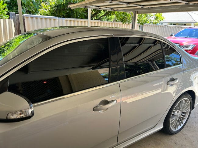 Silver sedan with professional window tinting parked under carport – enhances privacy, UV protection, and style.